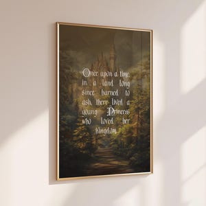 May include: A framed print with a gold border, featuring a fairytale scene of a castle in a forest. The text reads, "Once upon a time, in a land long since burned to ash, there lived a young Princess who loved her Kingdom."