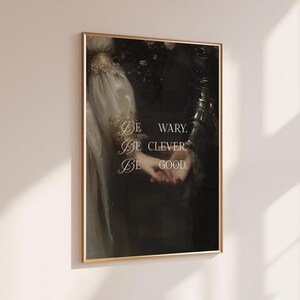 Puede incluir: Un cuadro enmarcado con una pintura de estilo vintage de dos figuras tomadas de la mano. La obra de arte tiene una est&eacute;tica oscura y melanc&oacute;lica con detalles dorados y el texto "Be wary. Be clever. Be good."