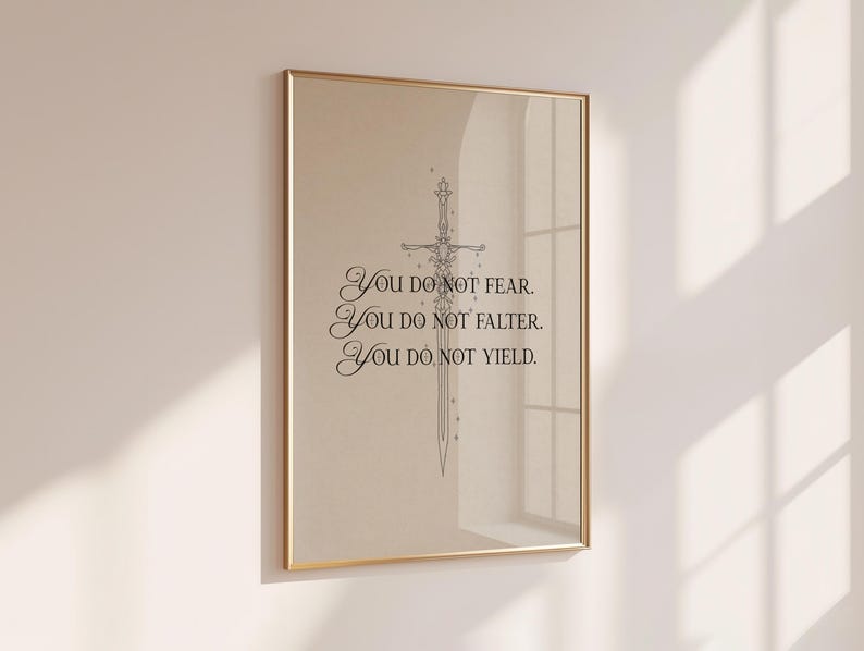 Może przedstawiać: Oprawiony wydruk ze złotą ramą, przedstawiający ilustrację miecza i tekst "YOU DO NOT FEAR. YOU DO NOT FALTER. YOU DO NOT YIELD." Grafika jest wyświetlana na beżowym tle.