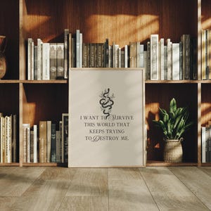 May include: A framed print with the text "I want to survive this world that keeps trying to destroy me." The print features a black snake and floral design. The print is displayed on a wooden floor in front of a bookshelf.