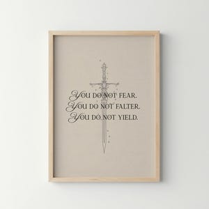 Może przedstawiać: Oprawiony wydruk z jasnobeżowym tłem i drewnianą ramą. Grafika przedstawia szczeg&oacute;łowy czarny rysunek linii miecza oraz tekst "You do not fear. You do not falter. You do not yield."