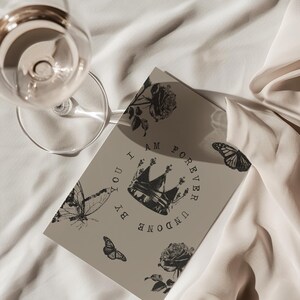May include: A greeting card with a crown and butterfly design. The card has the words "I AM FOREVER UNDONE BY YOU" printed on it. A wine glass is in the upper left corner.