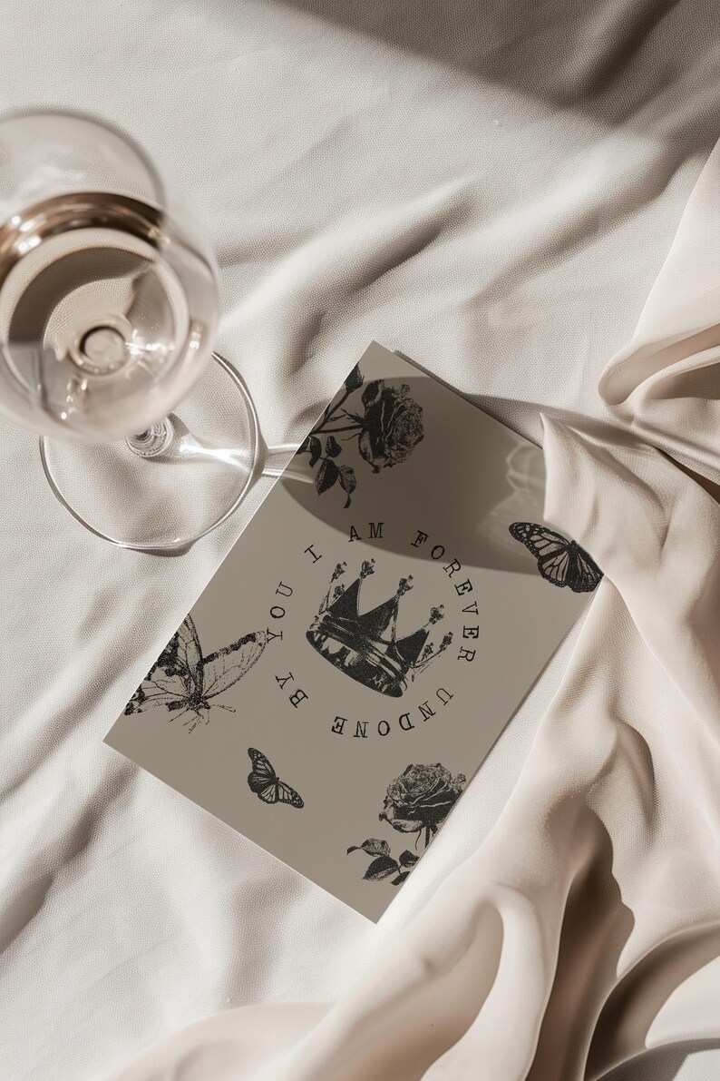 May include: A greeting card with a crown and butterfly design. The card has the words "I AM FOREVER UNDONE BY YOU" printed on it. A wine glass is in the upper left corner.