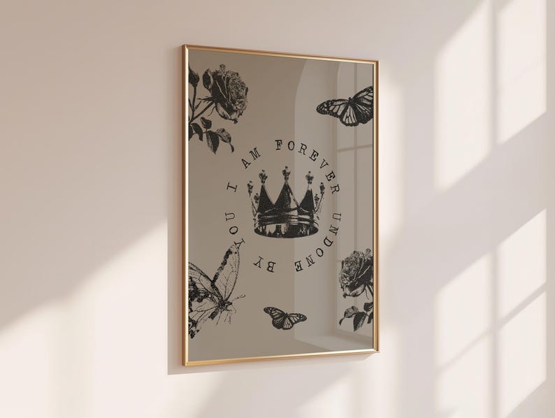 May include: A framed print with a gold border. The print features a crown, roses, and butterflies in black and white. The text "I AM FOREVER UNDONE BY YOU" is printed around the crown. The print is displayed on a beige wall.
