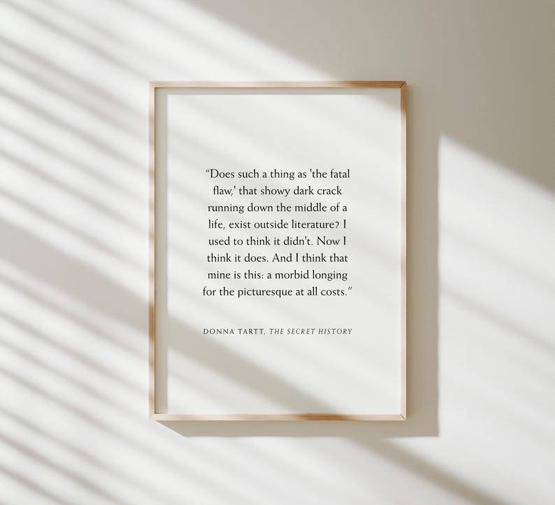 May include: A framed print with a light wood frame. The print features a quote from Donna Tartt's "The Secret History" in black text on a white background. The quote explores the concept of a 'fatal flaw' and a 'morbid longing'.