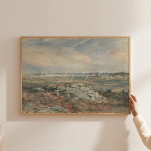 Op de afbeelding: Een ingelijste landschapsafdruk met een gedempt kleurenpalet van blauw, bruin en groen. Het kunstwerk toont een kustlandschap met een bewolkte lucht en rotsachtig terrein. De tekst "Keep reaching out your hand" staat over de afbeelding.