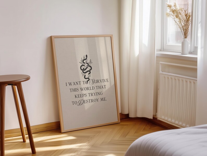 May include: A framed art print with a beige background and a wooden frame. The print features a black snake illustration with botanical accents and the text: "I WANT TO SURVIVE THIS WORLD THAT KEEPS TRYING TO DESTROY ME."