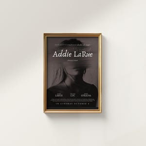 K&ouml;nnte beinhalten: Ein Filmplakat mit goldenem Rahmen. Das Plakat ist f&uuml;r einen Film namens "The Remarkable Life of Addie LaRue." Das Plakat zeigt ein Schwarzwei&szlig;foto eines Frauen Gesichts. Der Text "In Cinemas October 8" befindet sich am unteren Rand des Plakats.