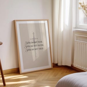 Może przedstawiać: Oprawiony wydruk z beżowym tłem i ilustracją miecza. Tekst brzmi: &bdquo;You do not fear. You do not falter. You do not yield.&rdquo; Rama jest w jasnobrązowym kolorze. Wydruk opiera się o ścianę.
