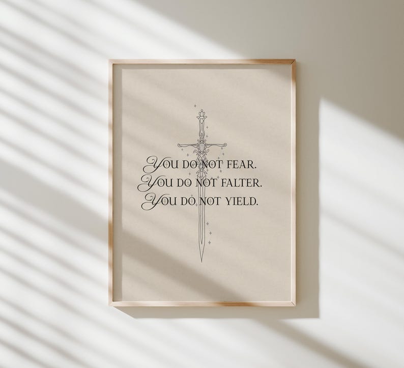 Może przedstawiać: Oprawiony wydruk z jasnobeżowym tłem. Zawiera szczeg&oacute;łowy rysunek linii miecza i tekst "YOU DO NOT FEAR. YOU DO NOT FALTER. YOU DO NOT YIELD." Rama jest w jasnym kolorze drewna. Idealny do dekoracji wnętrz.