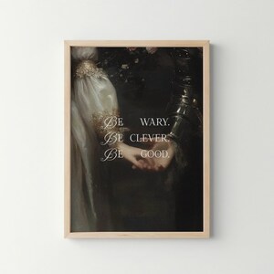 Puede incluir: Impresi&oacute;n art&iacute;stica enmarcada que presenta una pintura de estilo vintage con una est&eacute;tica oscura y melanc&oacute;lica. La obra representa figuras con ropa de &eacute;poca, con las palabras "Be wary. Be clever. Be good." en escritura elegante. El marco es de madera clara.