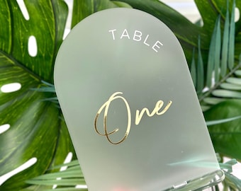 May include: A frosted green acrylic table number with a gold 'One' and the word 'TABLE' in white lettering.