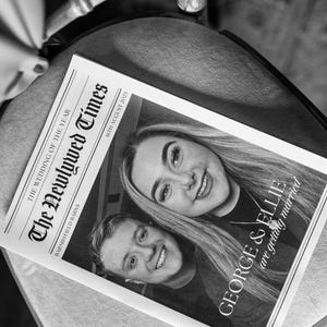 May include: Black and white photograph of a newspaper titled "The Newlywed Times" with the headline "The Wedding of the Year." The newspaper features two smiling people and the text "GEORGE & ELLIE are getting married" and "16th August 2025."