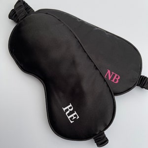 May include: Two black satin sleep masks with personalized initials. One mask has the initials "RE" in white and the other has the initials "NB" in pink.