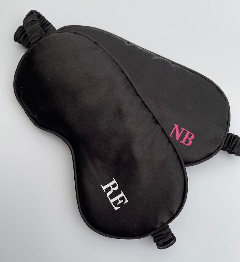 May include: Two black satin sleep masks with personalized initials. One mask has the initials "RE" in white and the other has the initials "NB" in pink.