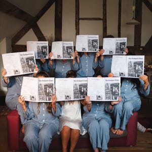 May include: A group of people in blue and white striped pajamas holding up newspapers with the headline "The Druidport Times". They are seated on a red couch in a room with exposed wooden beams.