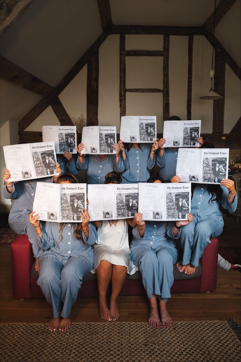 May include: A group of people in blue and white striped pajamas holding up newspapers with the headline "The Druidport Times". They are seated on a red couch in a room with exposed wooden beams.