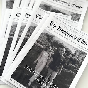 May include: A stack of black and white newspapers titled "The Newlywed Times." The front page features a photo of a couple and the text "MATTHEW & HOLLY are getting married." The date "20th JUNE 2025" is also visible.