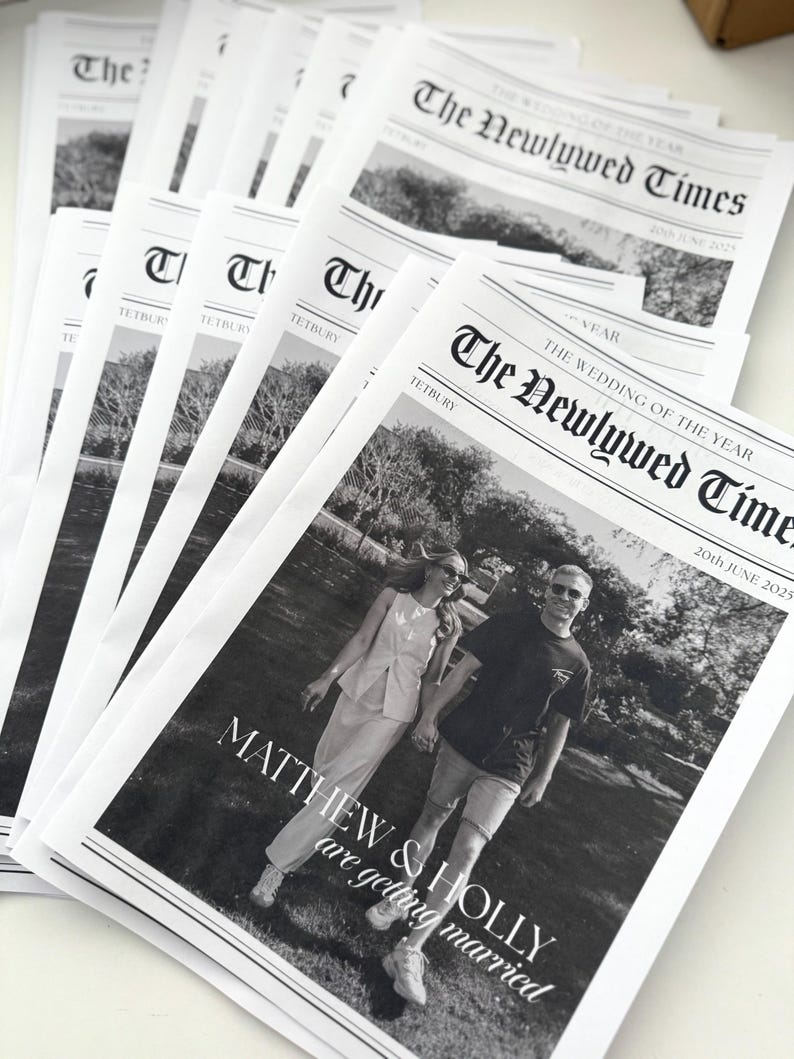 May include: A stack of black and white newspapers titled "The Newlywed Times." The front page features a photo of a couple and the text "MATTHEW & HOLLY are getting married." The date "20th JUNE 2025" is also visible.
