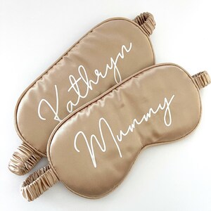 May include: Two gold satin sleep masks with white embroidered text. The top mask says "Kathryn" and the bottom mask says "Mummy".