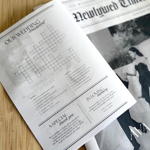 May include: Two wedding-themed newspapers are displayed. One features a crossword puzzle titled "OUR WEDDING crossword" with clues. The other newspaper is titled "THE WEDDING OF THE YEAR Newlywed Times" with a photo and text.