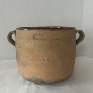 May include: A large, brown earthenware pot with two handles. The pot has a stamp on the side that reads "Ecurie Generale Vallauris Made".