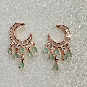 Puede incluir: Un par de pendientes de oro rosa con un diseño de media luna y piedras verdes en forma de lágrima que cuelgan.