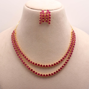 Peut inclure: Un ensemble collier et boucles d'oreilles dorées. Le collier présente deux rangées de pierres rondes de couleur rubis. Les boucles d'oreilles assorties sont composées de plusieurs pierres de couleur rubis. Les bijoux sont présentés sur un mannequin.