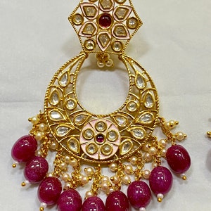 May include: Gold earrings with a pink and white enamel flower design, a crescent moon shape, and a dangling chain of burgundy beads.