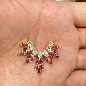 May include: A gold-toned jewelry connector featuring a fan-shaped arrangement of marquise-cut fuchsia stones and round clear stones. The piece has two small loops at the top for attachment, with a symmetrical design radiating from a central stone.