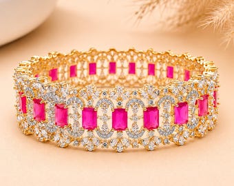May include: A gold-toned bangle bracelet featuring a repeating pattern of rectangular hot pink stones alternating with clusters of small, clear, sparkling white stones arranged in an intricate, openwork metal design that encircles the wrist.