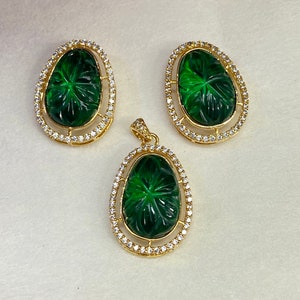 May include: A green gemstone pendant and earrings set with a carved floral design. The pendant and earrings are set in gold with a row of clear cubic zirconia stones around the perimeter.
