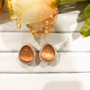 Puede incluir: Un par de pendientes de oro con una piedra naranja en forma de lágrima rodeada por un halo de brillantes transparentes.