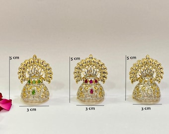 以下が含まれることがあります： 金色の装飾品が3つ。高さ5cm、幅3cm。花瓶のようなベースに透明と色の宝石が飾られ、詳細な葉の王冠のデザインが施されています。1つは緑、1つは赤、もう1つは色の宝石がありません。
