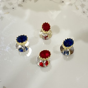 May include: Four cufflinks with a silver base and a red or blue gem in the centre. The gems are set in a gold crown-like design.