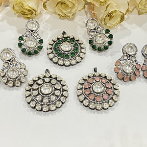 May include: A set of six silver pendant earrings and necklaces with intricate designs featuring white and clear stones. The pendants are circular and have a variety of colored accents, including green and pink.