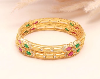 May include: A gold-toned bangle bracelet featuring a repeating openwork pattern. The design is accented with alternating marquise-cut pink and green stones, interspersed with small clear round stones set along the metal frame.