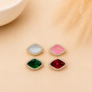 May include: Four marquise-shaped stud earrings arranged in a square. Each earring features a central faceted gemstone in white, pink, green, or red, surrounded by a border of small clear pavé stones set in a gold-toned metal frame.