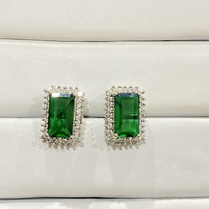 May include: A pair of emerald green rectangular earrings with a silver setting and a halo of small diamonds.