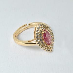 May include: A gold ring featuring a pink marquise-shaped stone set within a double row of clear cubic zirconia stones.
