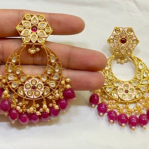 May include: A pair of gold earrings with pink and white enamel floral designs, surrounded by clear stones. The earrings have a dangling section of pink beads.