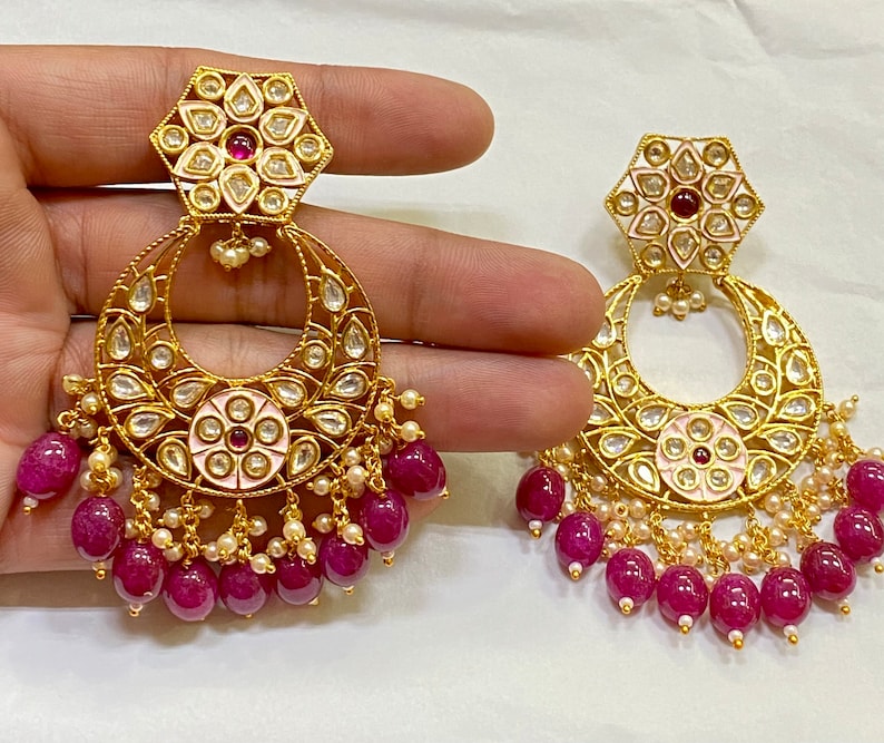 May include: A pair of gold earrings with pink and white enamel floral designs, surrounded by clear stones. The earrings have a dangling section of pink beads.