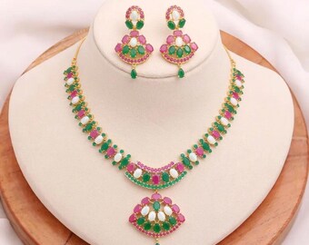 May include: A gold-toned jewelry set featuring a necklace and matching earrings. The necklace and earrings are adorned with green, pink, and white gemstones. The necklace has a pendant and the earrings are drop style.