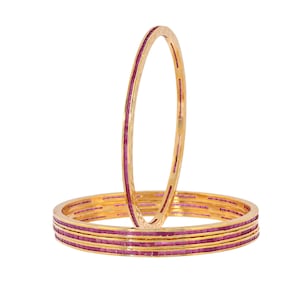 Può includere: Set di quattro braccialetti d'oro con intarsi di pietre rosa. I braccialetti sono impilati uno sopra l'altro.