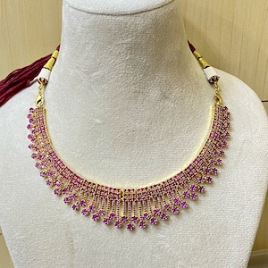 May include: A gold necklace with a pink stone design. The necklace has a delicate, layered look with multiple rows of small pink stones.