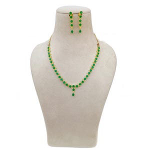 Puede incluir: Un conjunto de collar y pendientes dorados con piedras verdes esmeralda en forma de lágrima. El collar tiene un colgante central y los pendientes son colgantes. Las joyas se exhiben en un maniquí.
