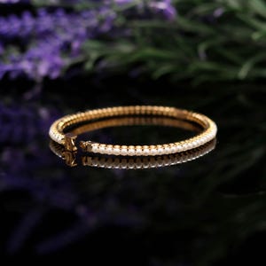 May include: A gold-toned bracelet with a row of small, white pearls. The bracelet is set against a dark background, with a reflection visible below. The clasp is visible, and the bracelet appears to be new.
