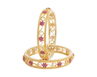May include: Two gold bangles with intricate floral designs and pink gemstones.