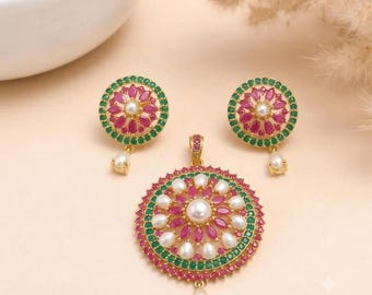 Può includere: Un set di gioielli color oro composto da un ciondolo circolare e orecchini abbinati. Ogni pezzo presenta una perla bianca centrale circondata da un anello di pietre rosa taglio marquise, un bordo esterno di pietre verdi e una perla pendente.
