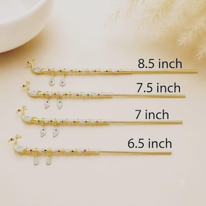 Könnte beinhalten: Vier goldfarbene Haarnadeln in Pfauenform, jeweils mit kleinen bunten Steinen und zwei hängenden Anhängern verziert. Die Längen sind mit 8.5 inch, 7.5 inch, 7 inch und 6.5 inch angegeben, was die Größe jedes einzelnen Haaraccessoires markiert.
